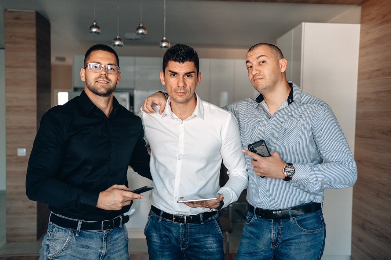 Group of three adult men with digital devices posing in a modern indoor setting.